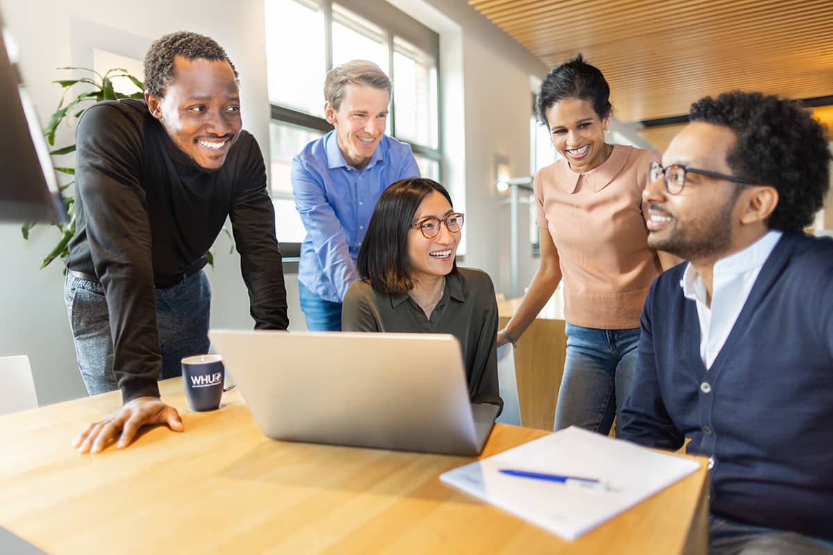 Fünf lächelnde MBA Studierende machen eine Gruppenarbeit am Notebook