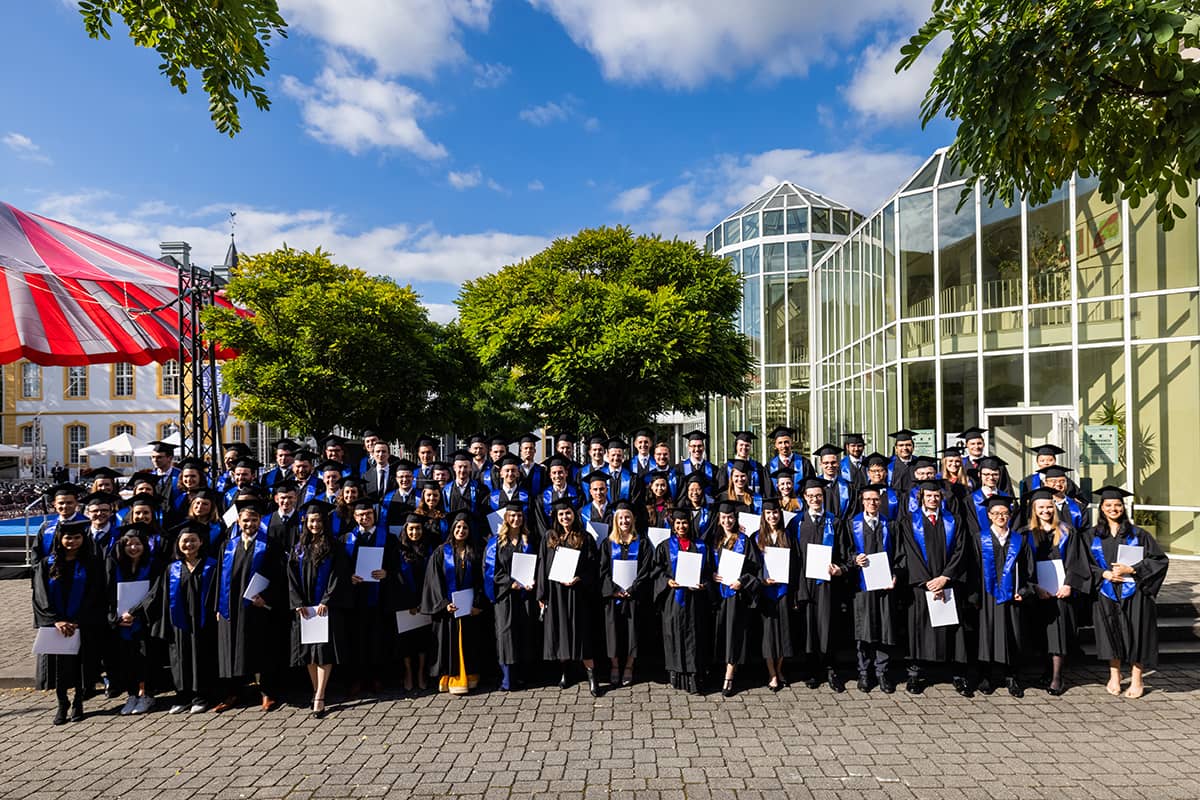 A group photo of Master graduates under a blue sky on the Burgplatz