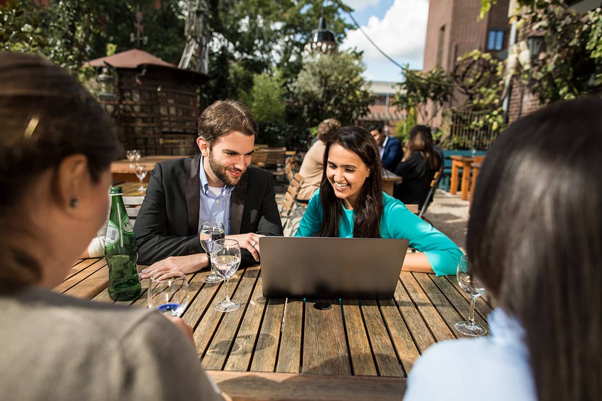 Ein männlicher und ein weiblicher Studierende sitzen draußen an einem Tisch und arbeiten an einem Notebook am WHU Campus Düsseldorf