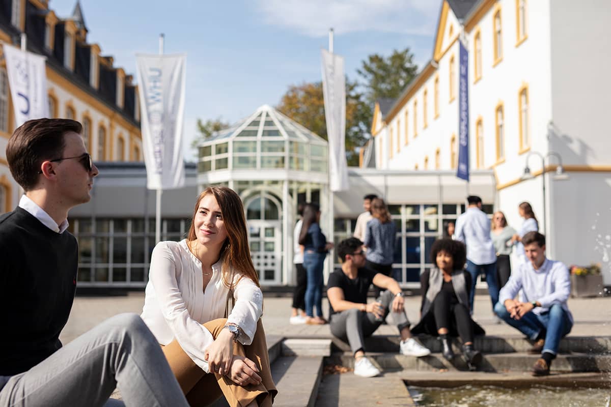 Students sit and chat in the sunshine on the Burgplatz at WHU Campus Vallendar